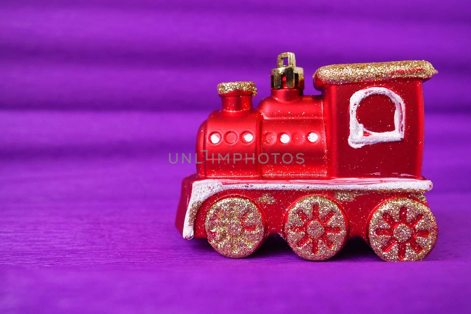 Red toy train locomotive on a purple and lilac gradient background. New Year or Christmas card. Icicles and snow on a train. Free space for text. Copy space. Festive background