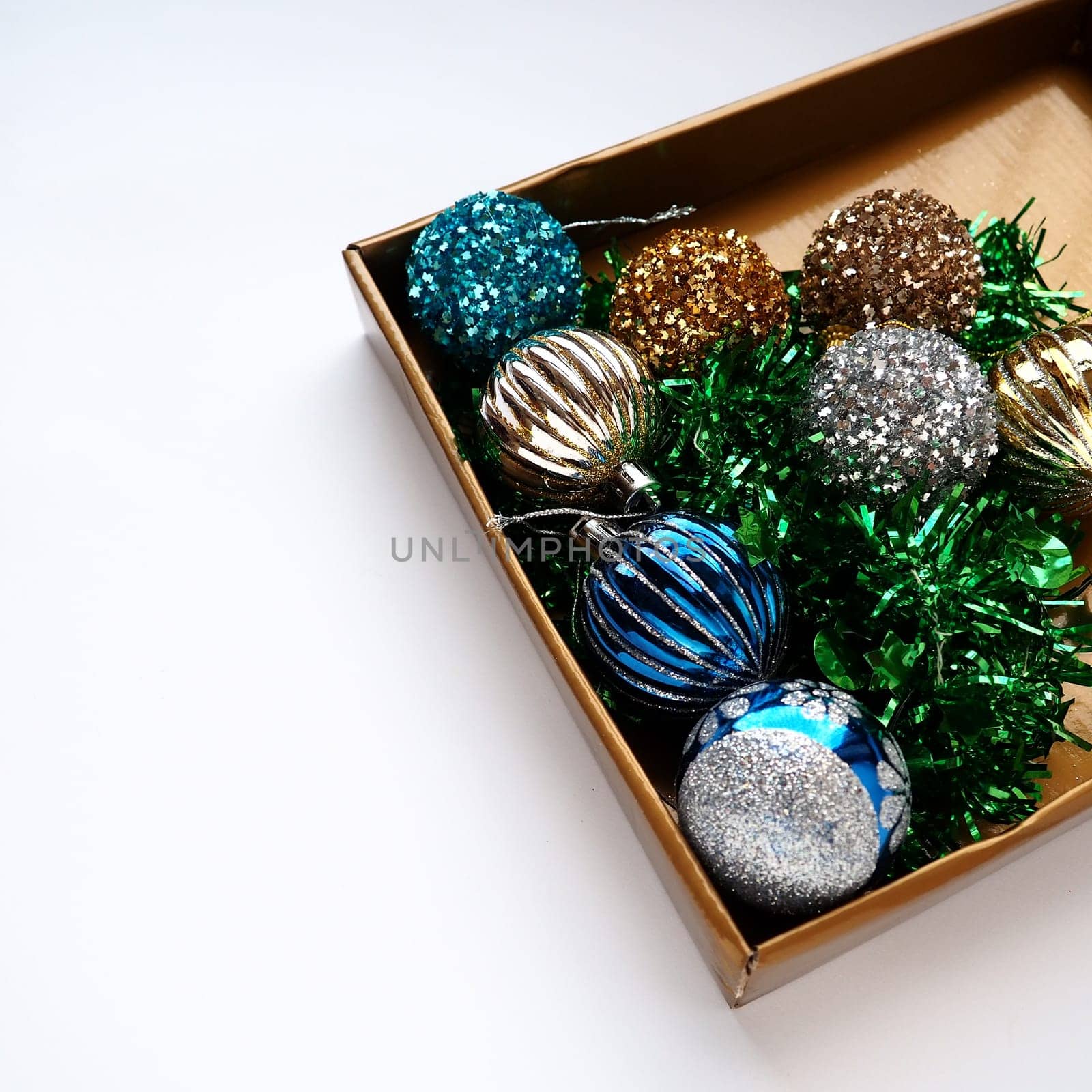 trendy Christmas decorations, colorful balls and tinsel in the lid of a gift box. Shiny beige or brown box for gifts or storage. New Year's Christmas card. Copy space. White background.
