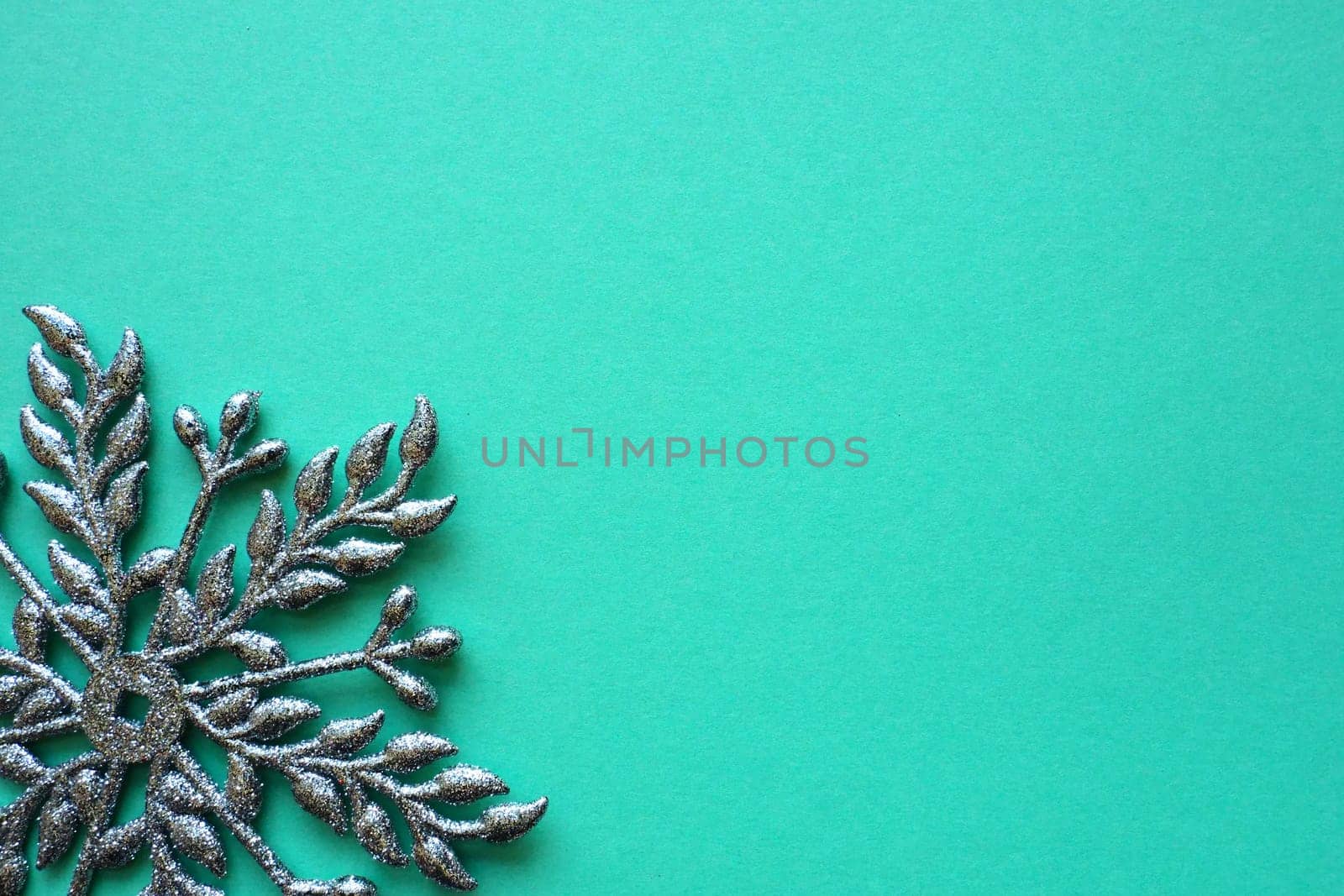 New Year or Christmas background with decorative snowflake around the edges of a sheet of colored paper. Copy space. Blue silver snowflake on a green background. Postcard, background or invitation.