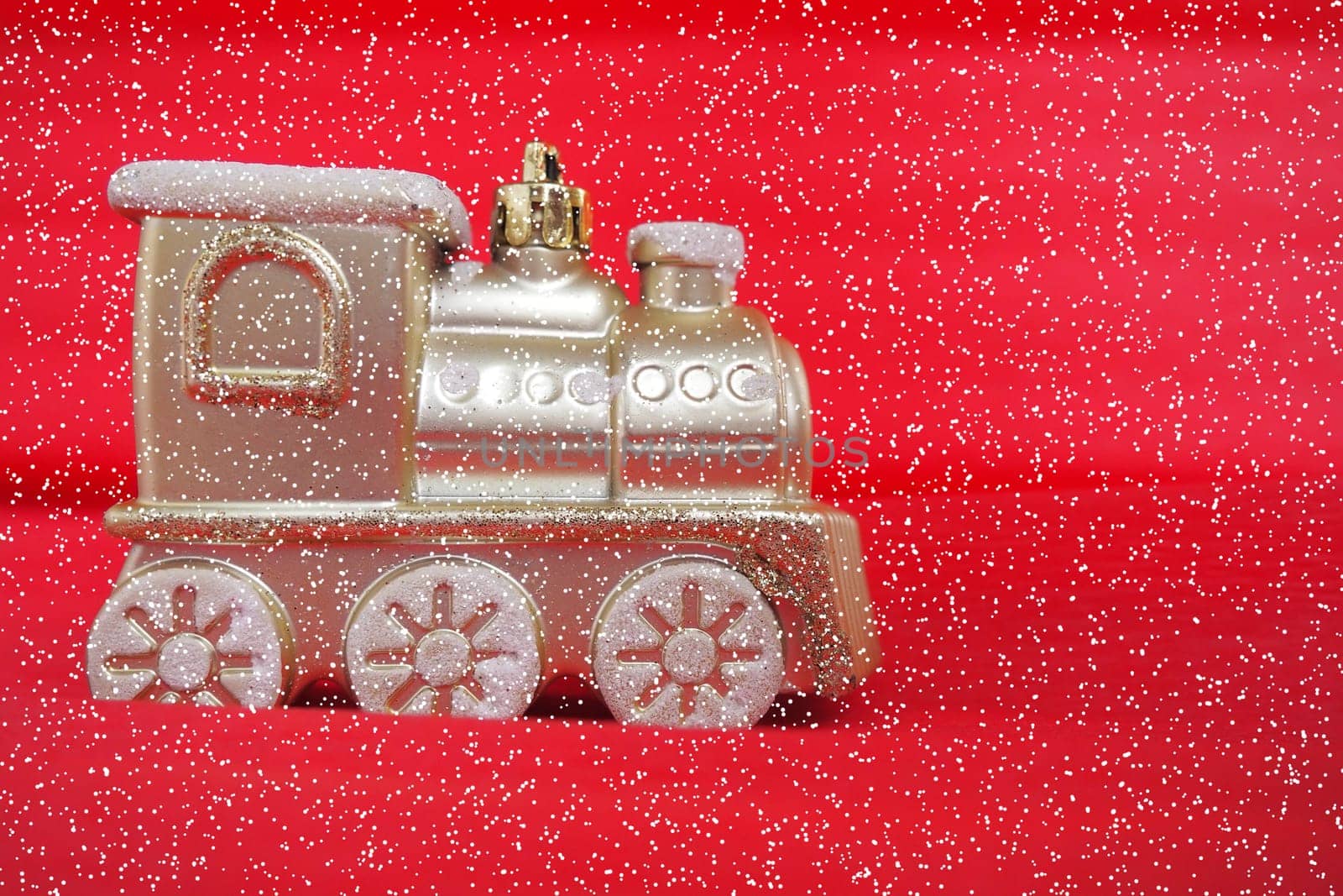 Golden toy train locomotive on a red and pink gradient background. New Year or Christmas card. Icicles and snow on a train. Free space for text. Copy space. Falling snowflakes