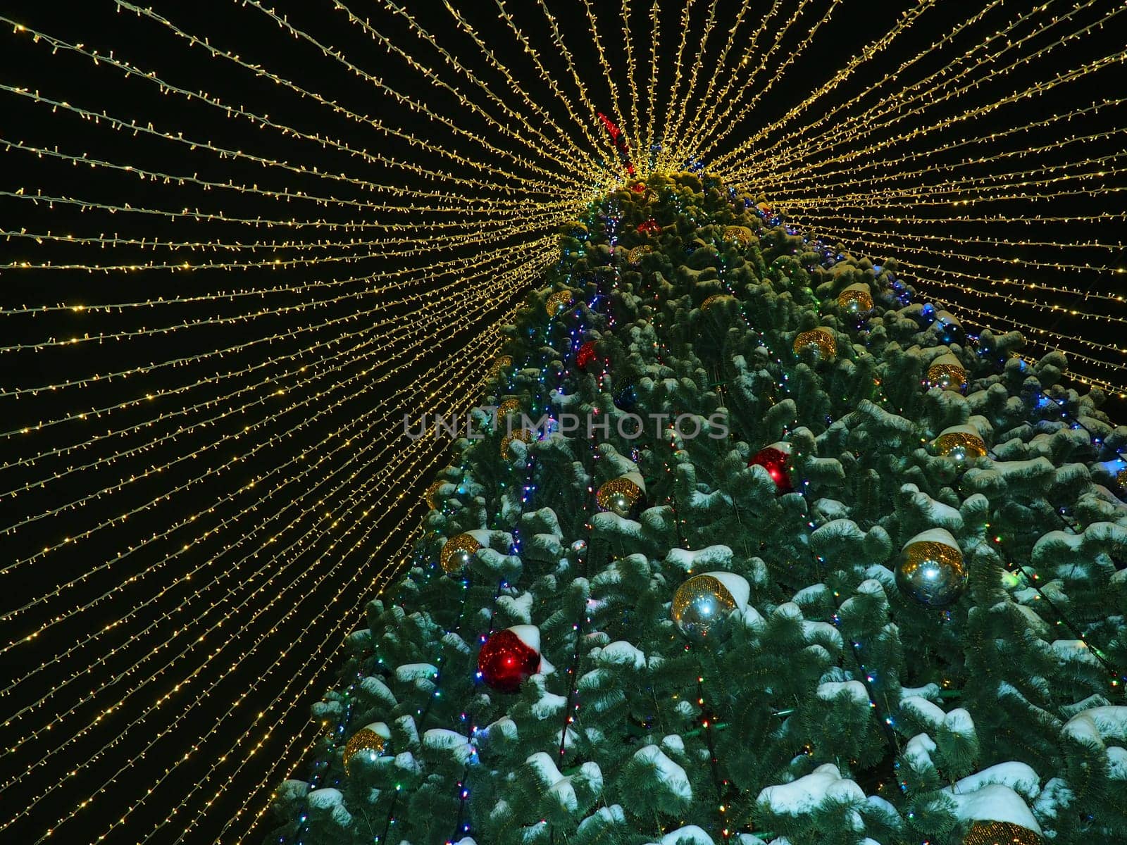 big beautiful Christmas Tree with decorations and Illuminations in snowy night. New Year and Christmas holiday background. Festive winter city landscape