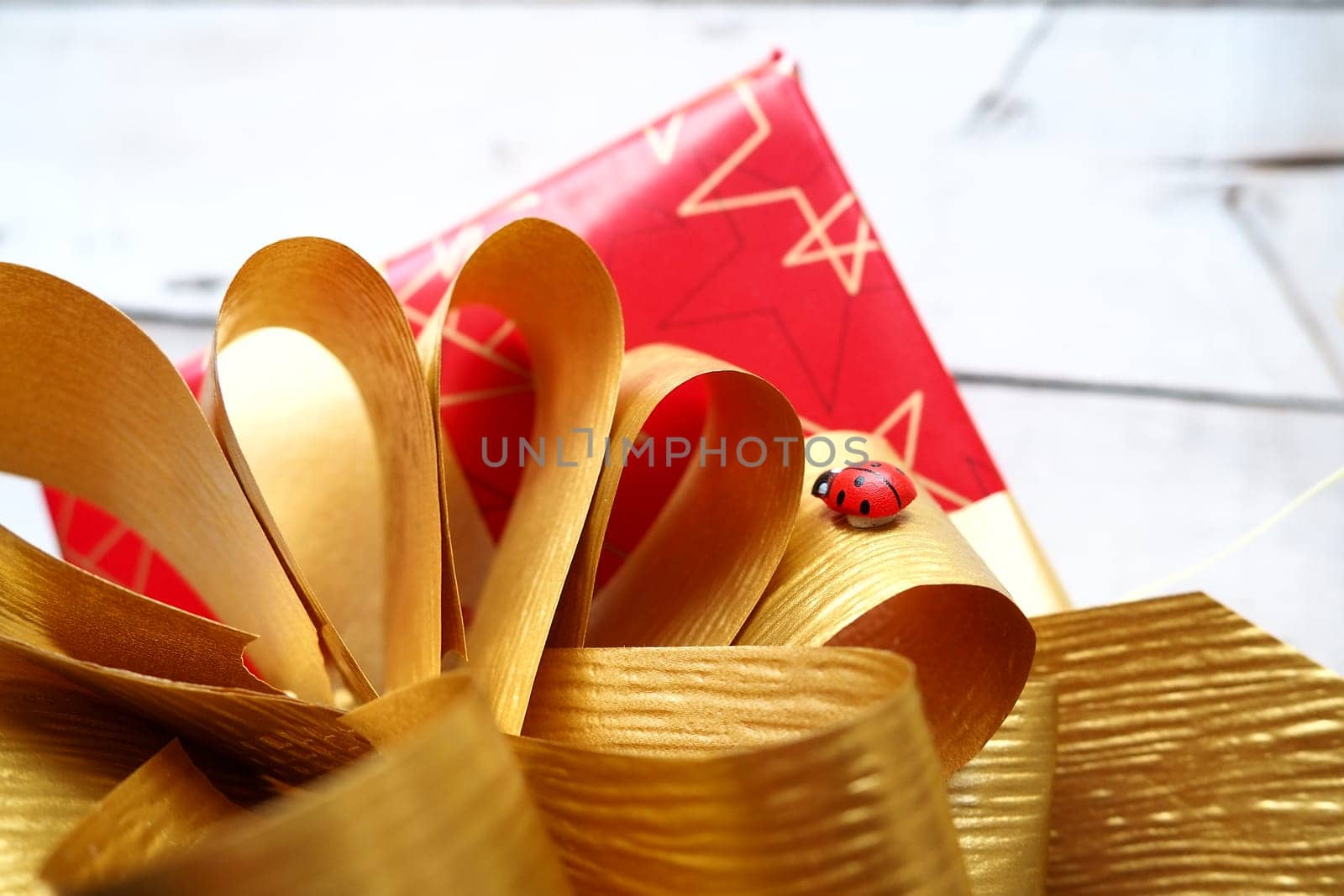Red gift box with a large gold bow on a wooden background painted with white paint. Gift for Christmas, New Year, Birthday, Mother's Day, Wedding, Valentine's Day. Beautiful festive decoration.