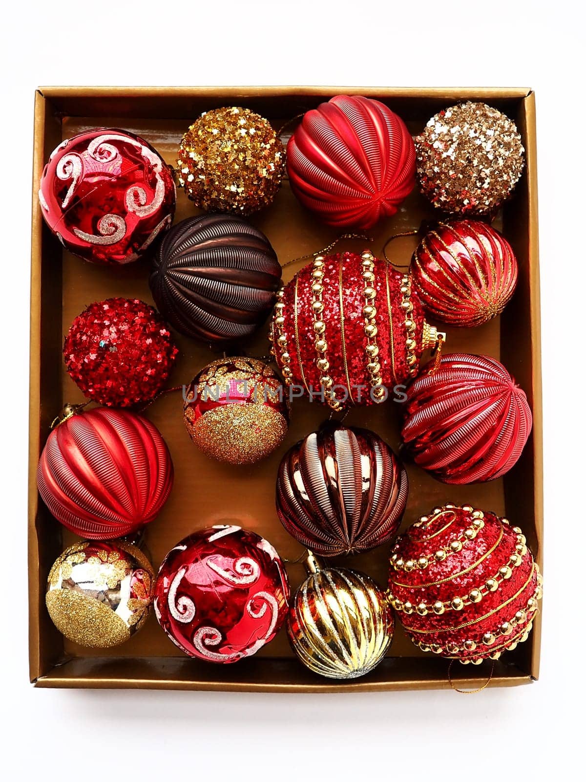 Christmas decorations in a box on a white background. Beautiful red and gold balls with sparkles and stripes. Preparing for the New Year Christmas holidays. Beautiful decorations. Copy space isolated