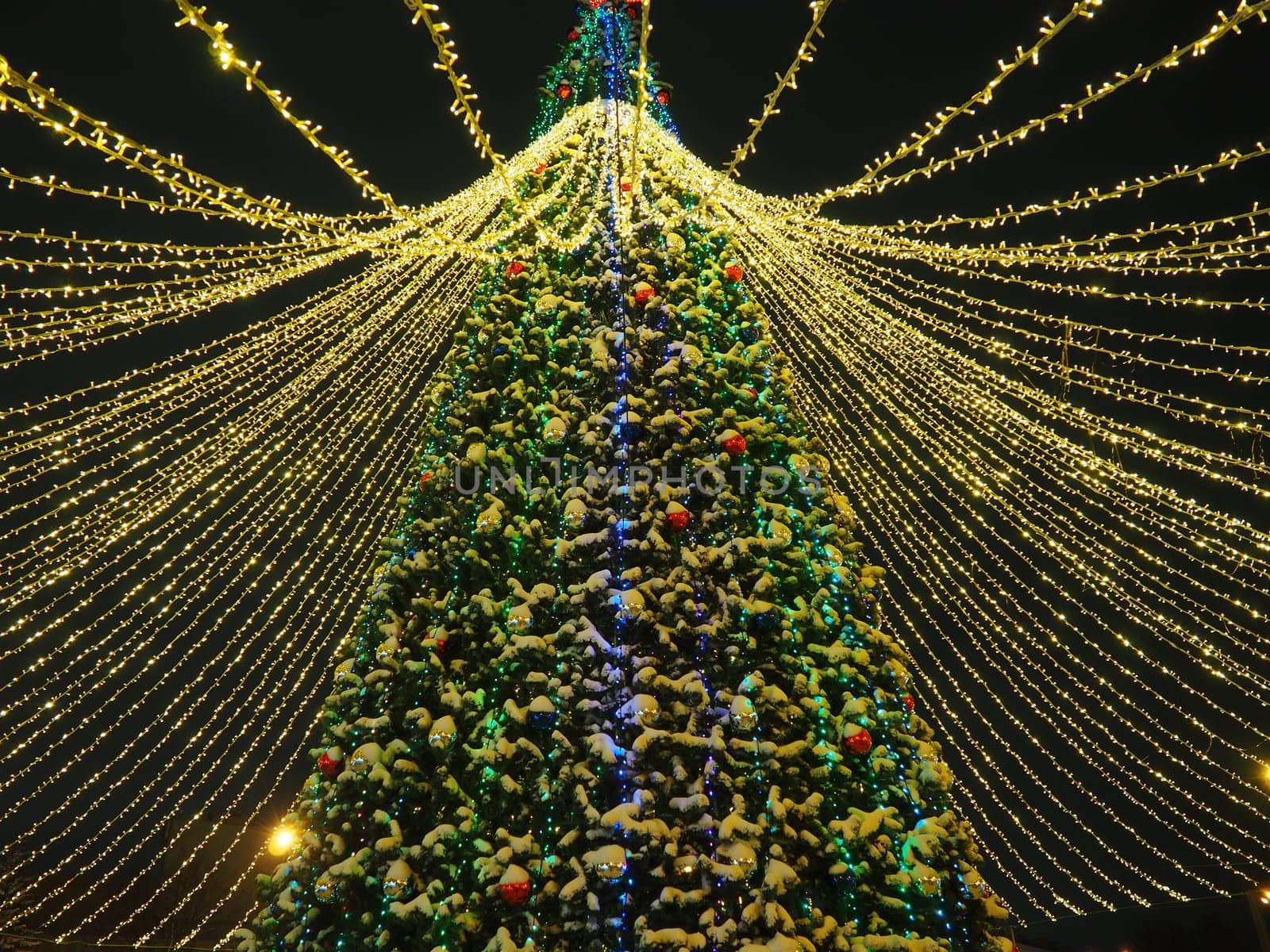 big beautiful Christmas Tree with decorations and Illuminations in snowy night. New Year and Christmas holiday background. Festive winter city landscape