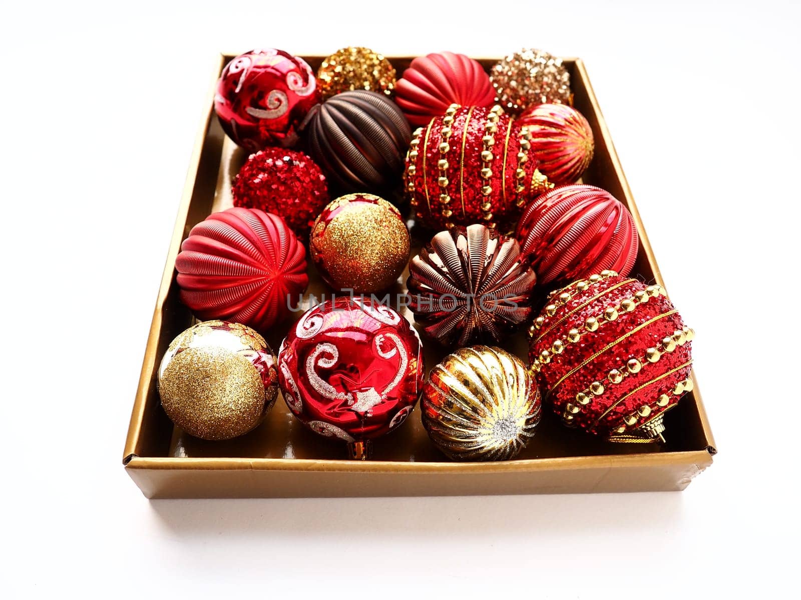 Christmas decorations in a box on a white background. Beautiful red and gold balls with sparkles and stripes. Preparing for the New Year Christmas holidays. Beautiful decorations. Copy space isolated