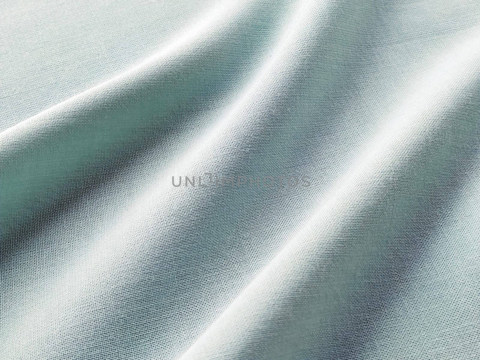 Beautifully folded fabric. Soft pleasant waves and flounces on textiles. Close-up. Drapery for curtains, fabric for dressmaking or upholstery. Green or blue color.
