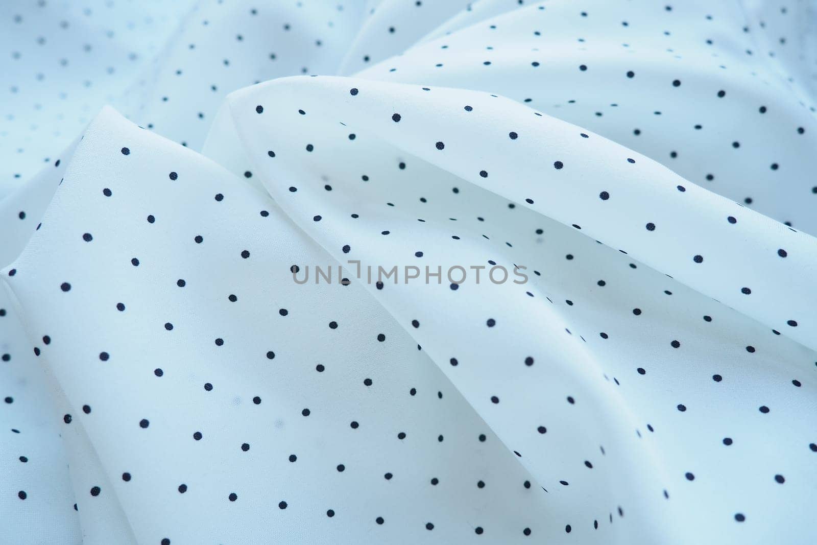 Texture of silk fabric. Black polka dots on a white background. Dress lightweight synthetic fabric in white with a repeating pattern. The textile is made up of waves and folds. Feminine classic style