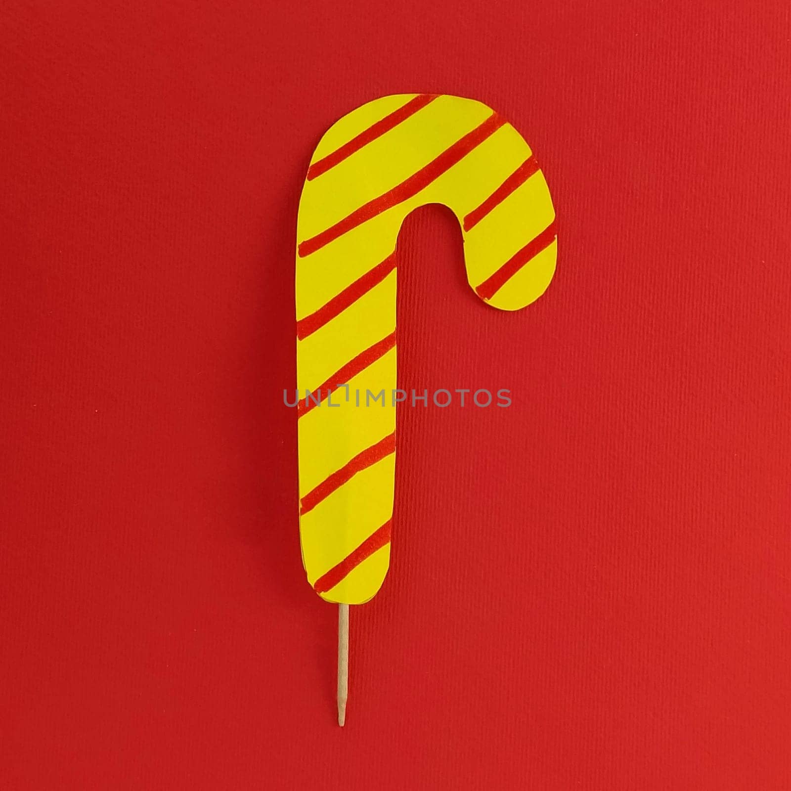 Lollipop on a red background. Imitation of yellow candy with red stripes. New Year or Christmas decoration. Copy space. Lollipop in the middle of the image.