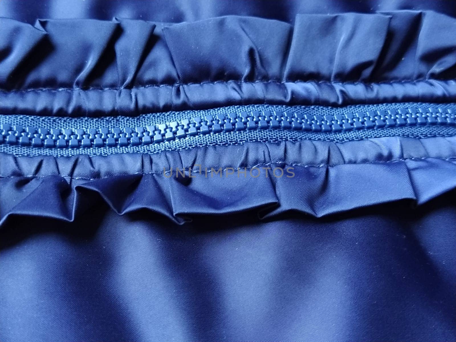 Buttoned zip on a blue raincoat. Waves and folds in the fabric. Beautiful flounces, ruffles, frills. Decorative finishing of a garment. Smocked, sewn silk fabric. Nice casual wear