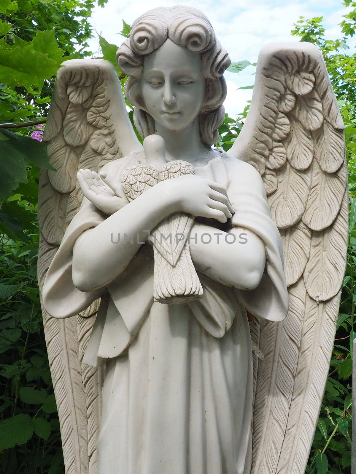 An angel with a dove. Sculpture in the cemetery. The figure of an angel with wings holding a bird in his arms. Lamentation for the deceased. Headstone monument on a Christian grave. Sadness sorrow