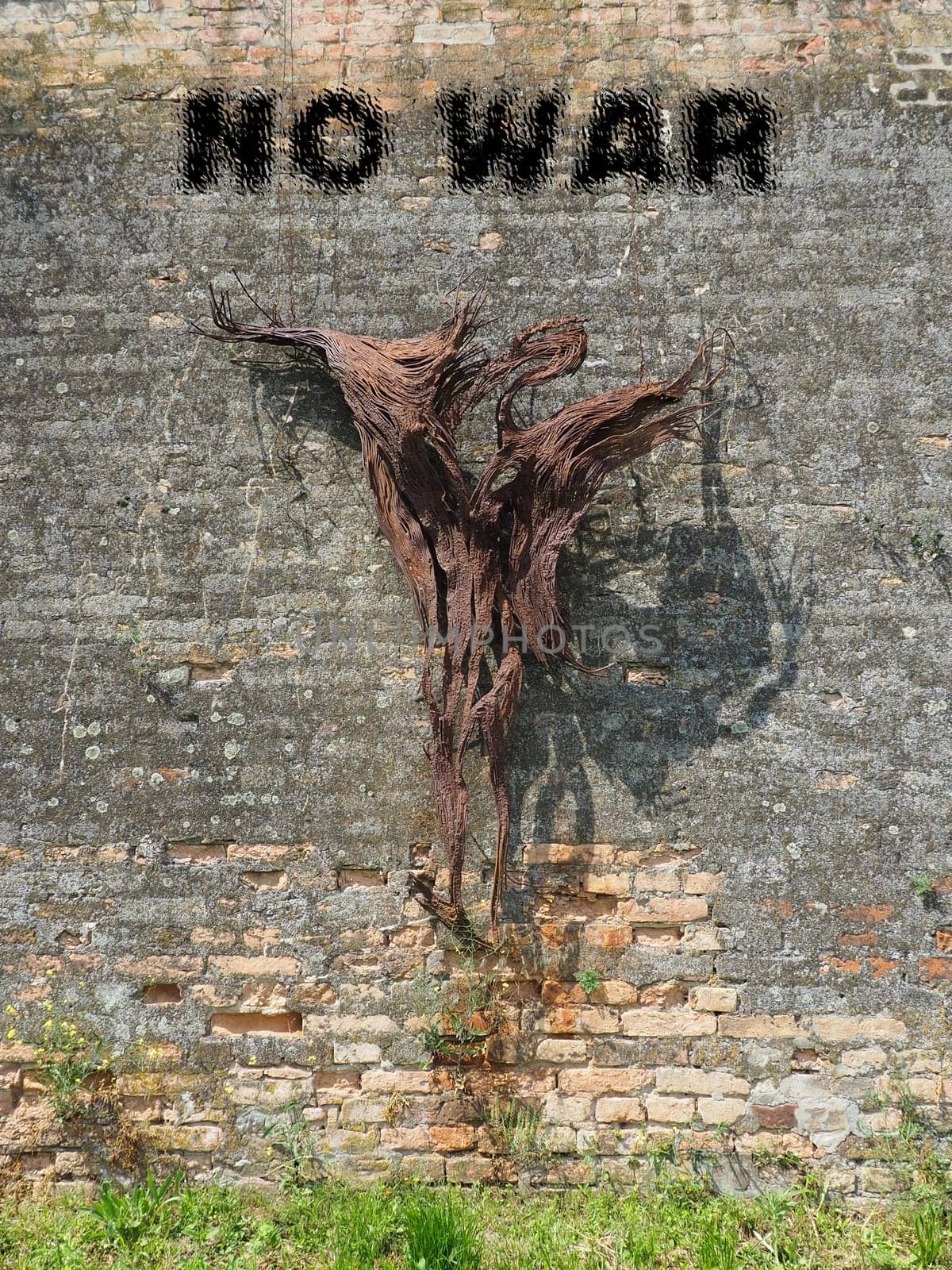 No war. Stop the war. Anti-war inscription in black. Brick background. A call to peace. Abstract silhouette of a man crucified on a wall, or burned in a nuclear explosion. Roots or bark of a tree.
