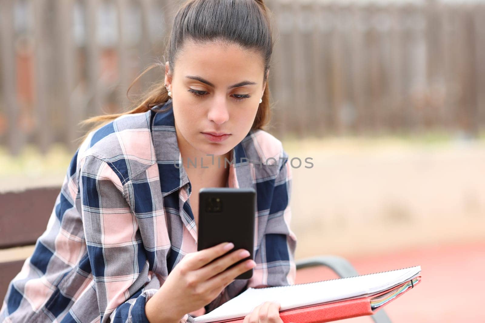 Student checking smart phone sitting in a park