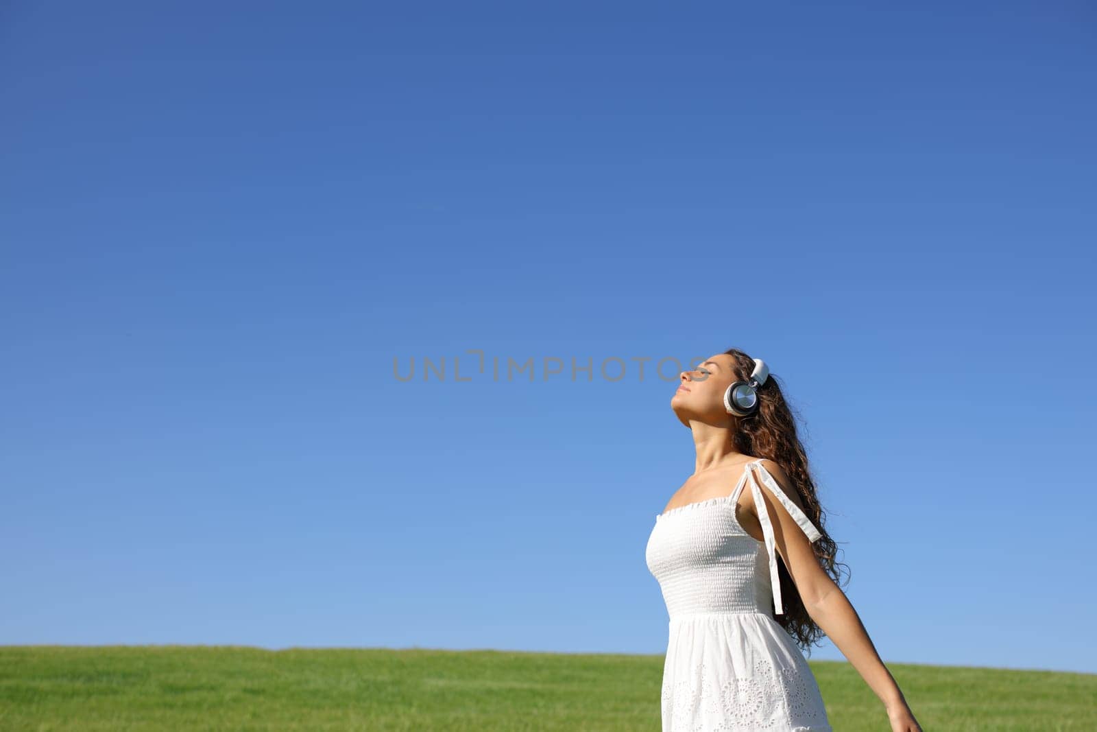 Woman meditating breathing fresh air with headphones in nature