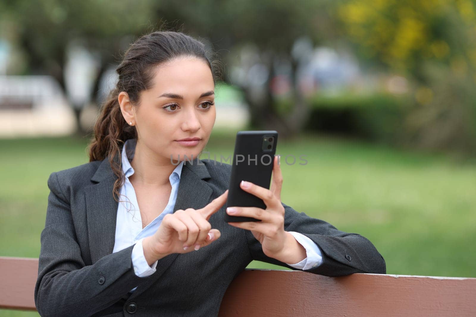 Businesswoman sitting in a bench in a park using phone