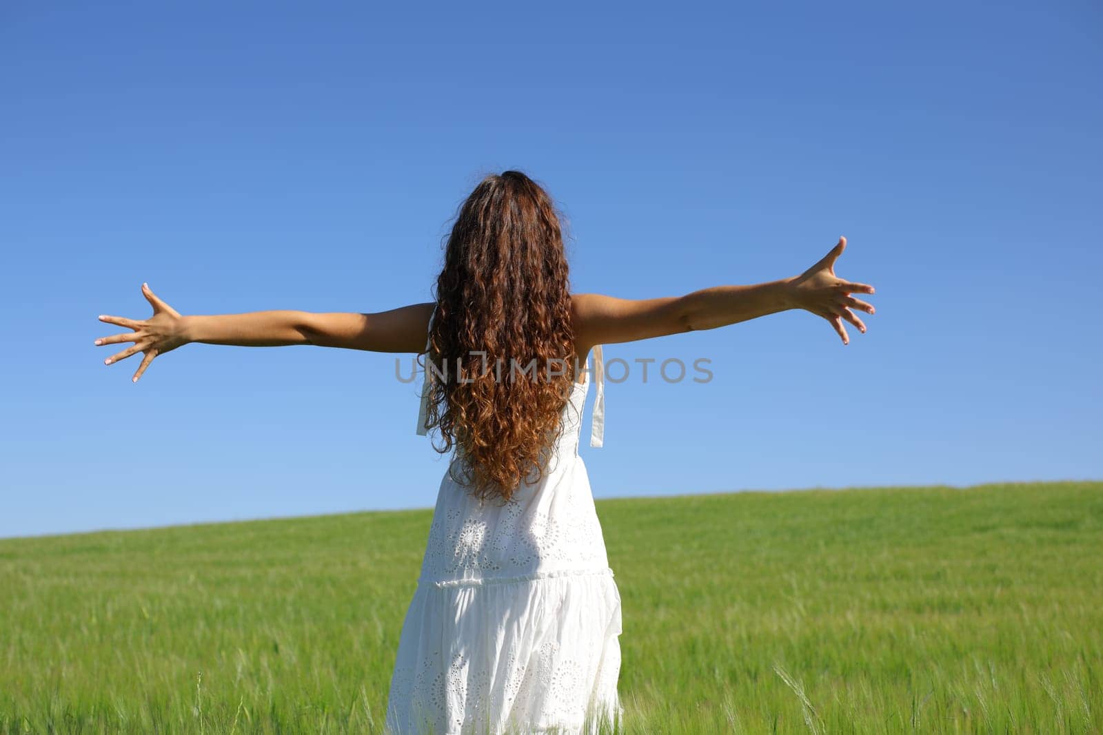 Back view portrait of a woman with white dress celebrating outstretching arms in a field