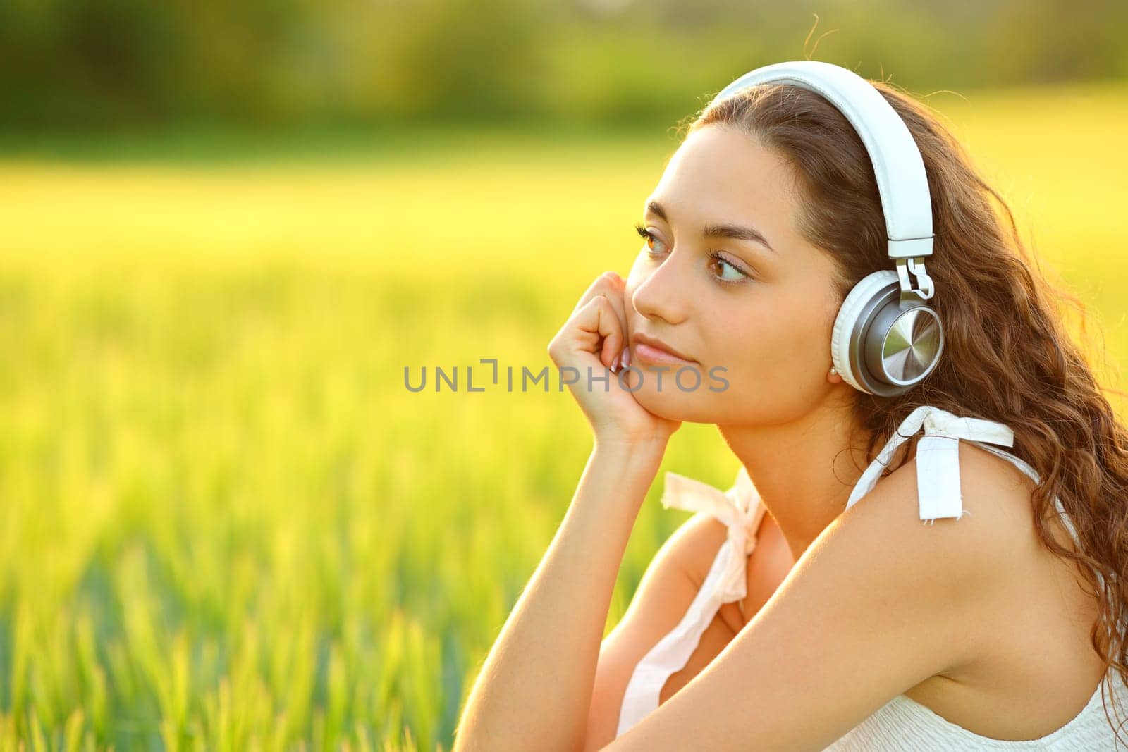 Woman thinking listening to music lookig away in a field at sunset