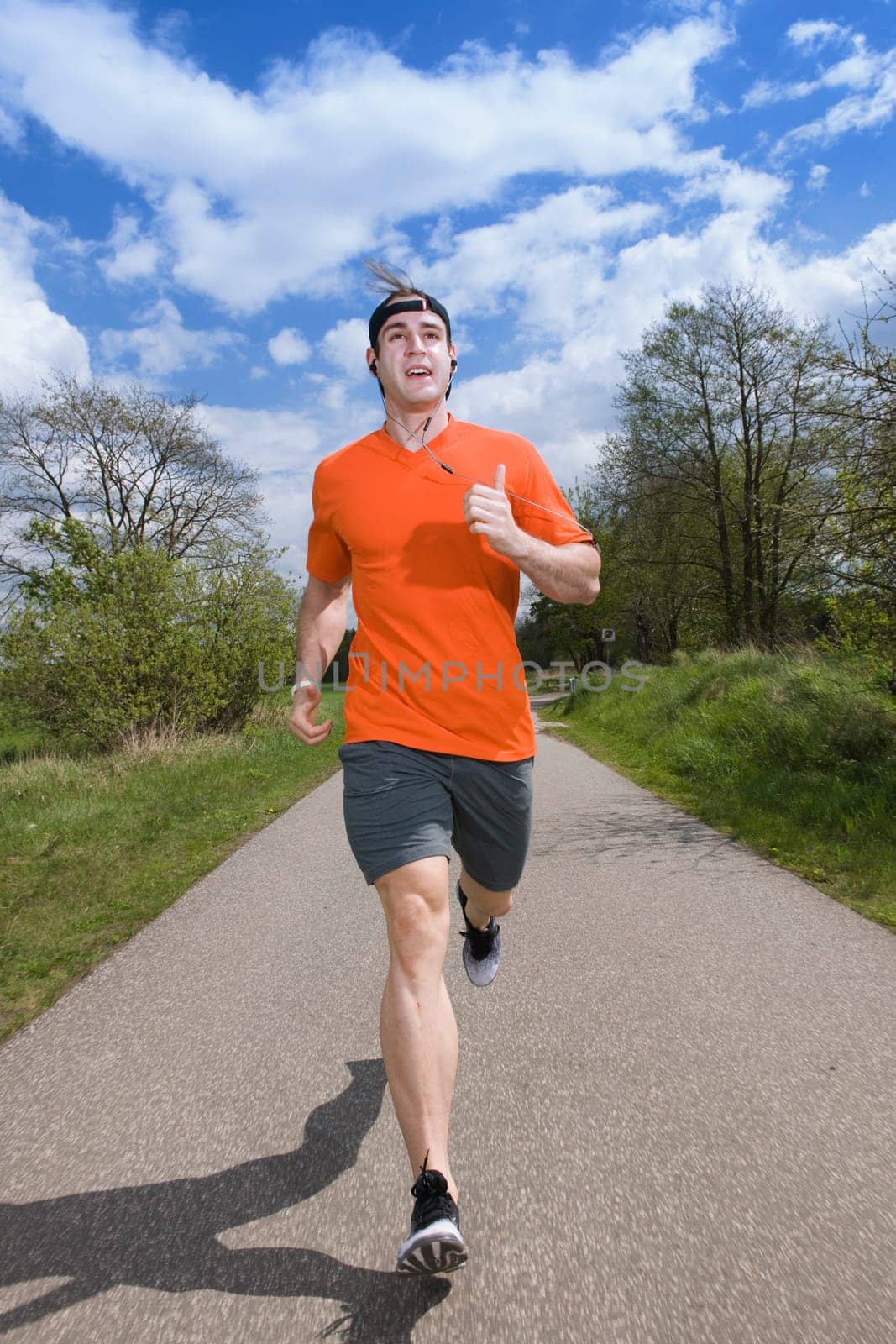 frontal full-body view of a young man in a sports dress jogging towards the camera on an asphalt road