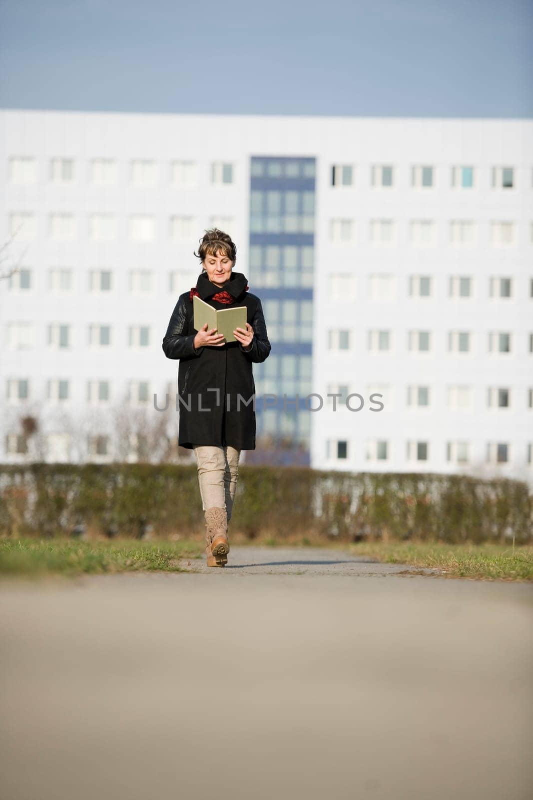 frontal full-body view of a mature woman in black leather jacket reading a book to the camera to go in front of white fuzzy plate construction in the background