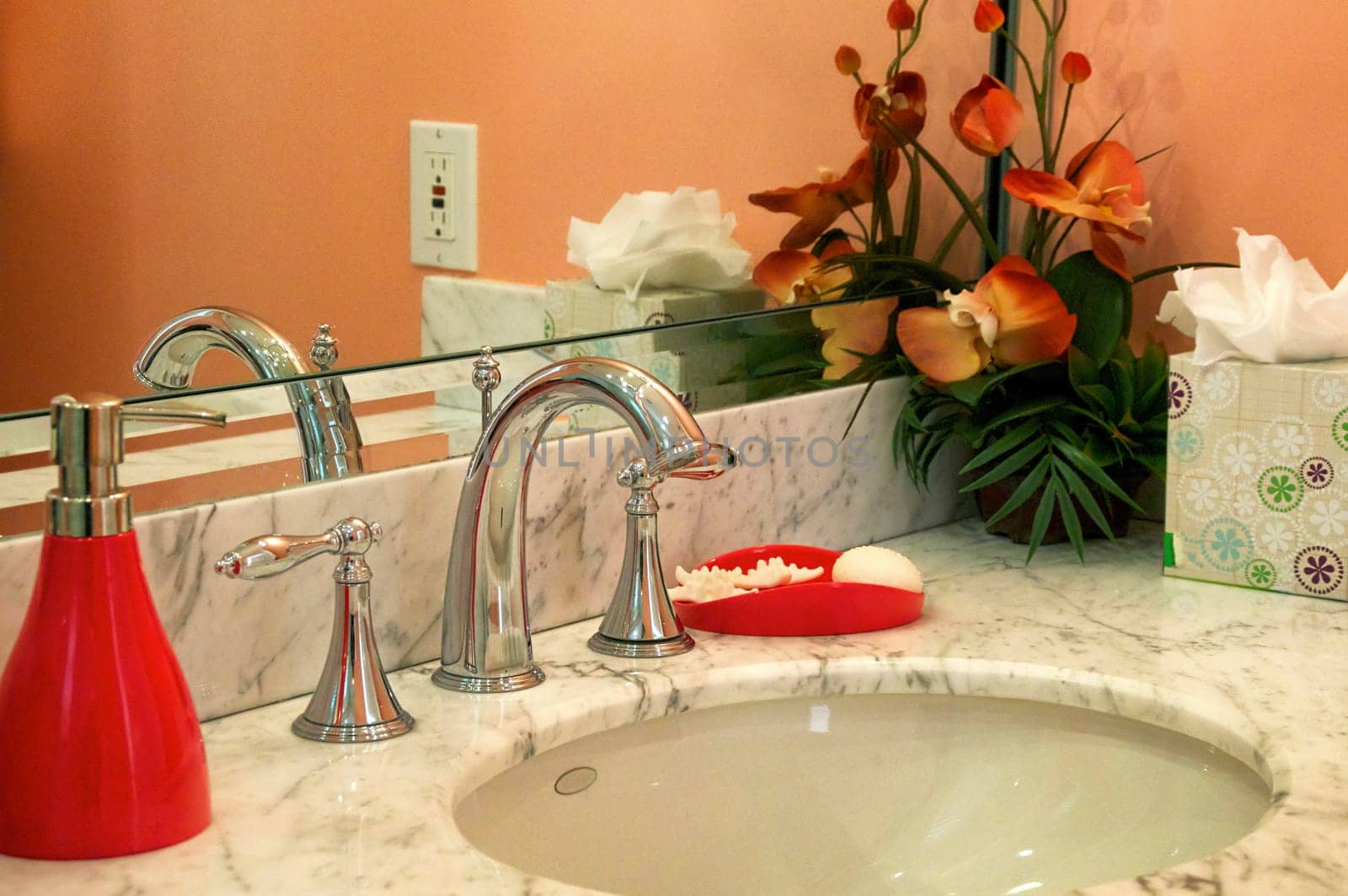 Detail of marble bathroom sink surrounded by orange walls and decor.