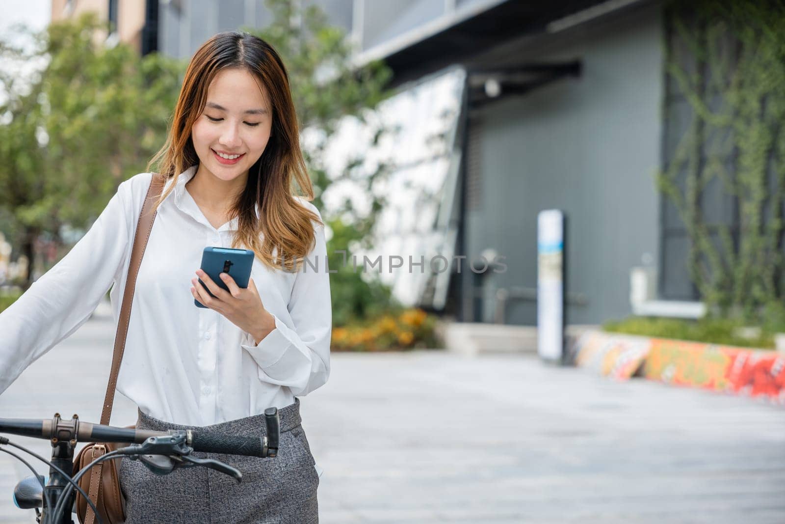 Portrait of beautiful smile business woman commute her bicycle outdoor using smartphone at urban, bike go to work office, Asian businesswoman standing on city street with bicycle holding mobile phone