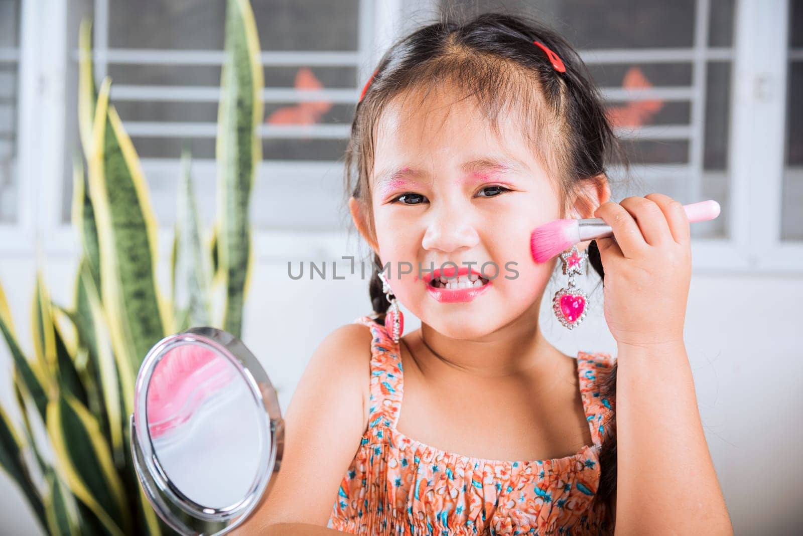 Happy kid is beautiful make up with cosmetics toy, Asian adorable funny little girl making makeup her face she looking in the mirror and cheek fluffy brush for powder, Learning activity to be woman