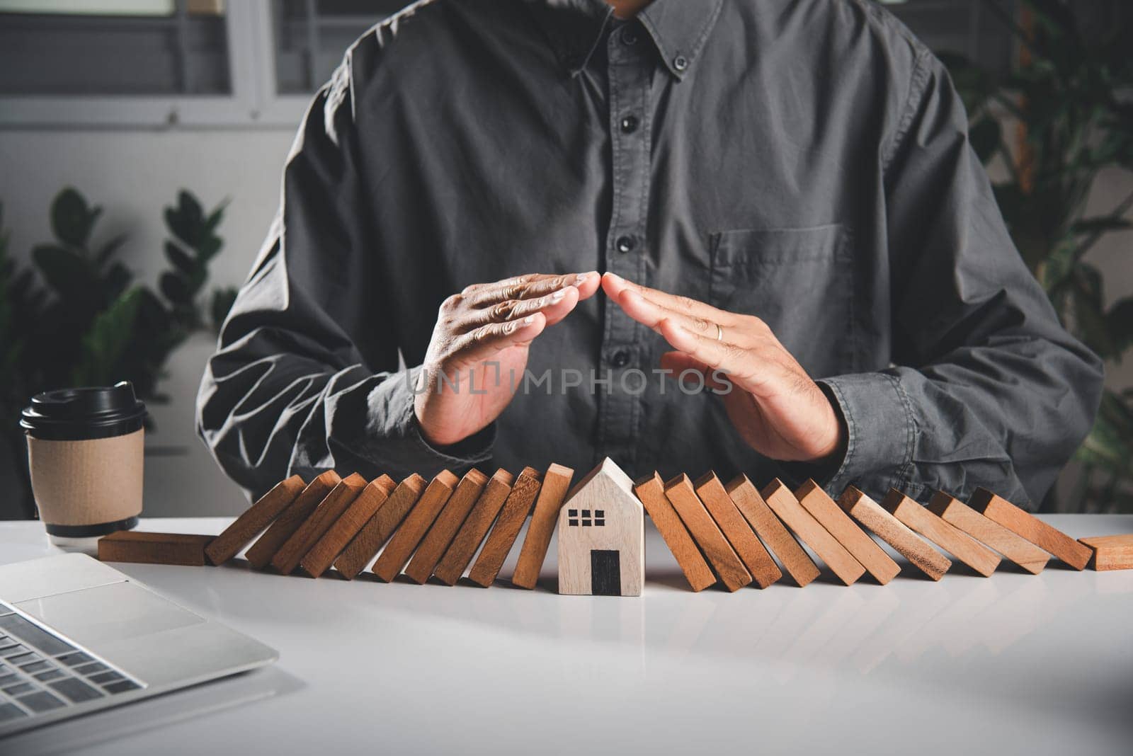 Business risk plan real estate protection. Man hand blocks wood block from many row falling wooden block like domino to house model, Insurance ideas to prevent loss concept
