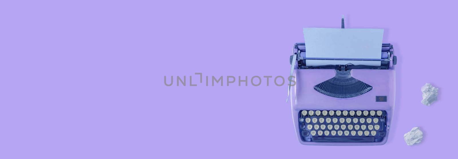 A violet vintage typewriter with violet background and two paper balls.
