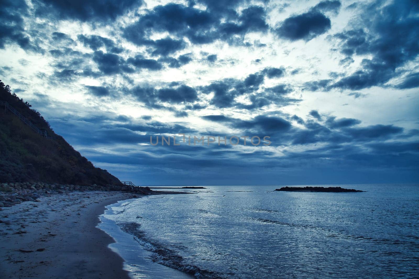 Sunset on the Danish coast. Beach, waves. Hill with trees in background. Landscape photo from sea