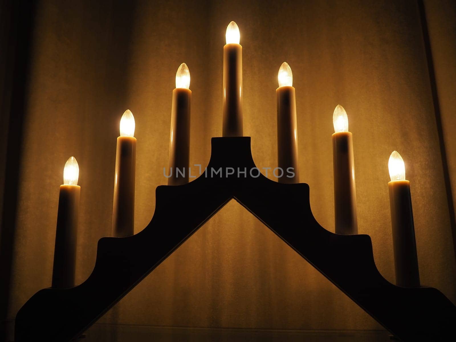 Schwibbogen arch luminaire in the form of a triangular candlestick. Yellow background. Evening, romantic, festive, religious or mystical atmosphere. Burning light bulbs that resemble candlelight.