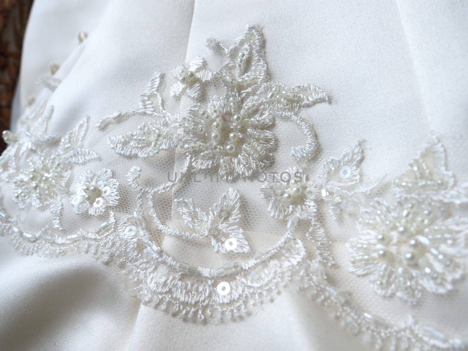Beaded embroidery and lace close-up on a white wedding dress. Beautiful jewelry for the bride's outfit. Wedding preparations. Clothes of the newlyweds. Small shiny details on the dress, handmade.