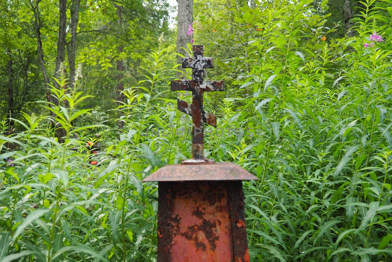 Metal cross on the grave. Monument in the form of a cross in the cemetery. Daytime in summer. The theme of grief, death and Halloween. Religious Christian symbol of the repose of the soul.