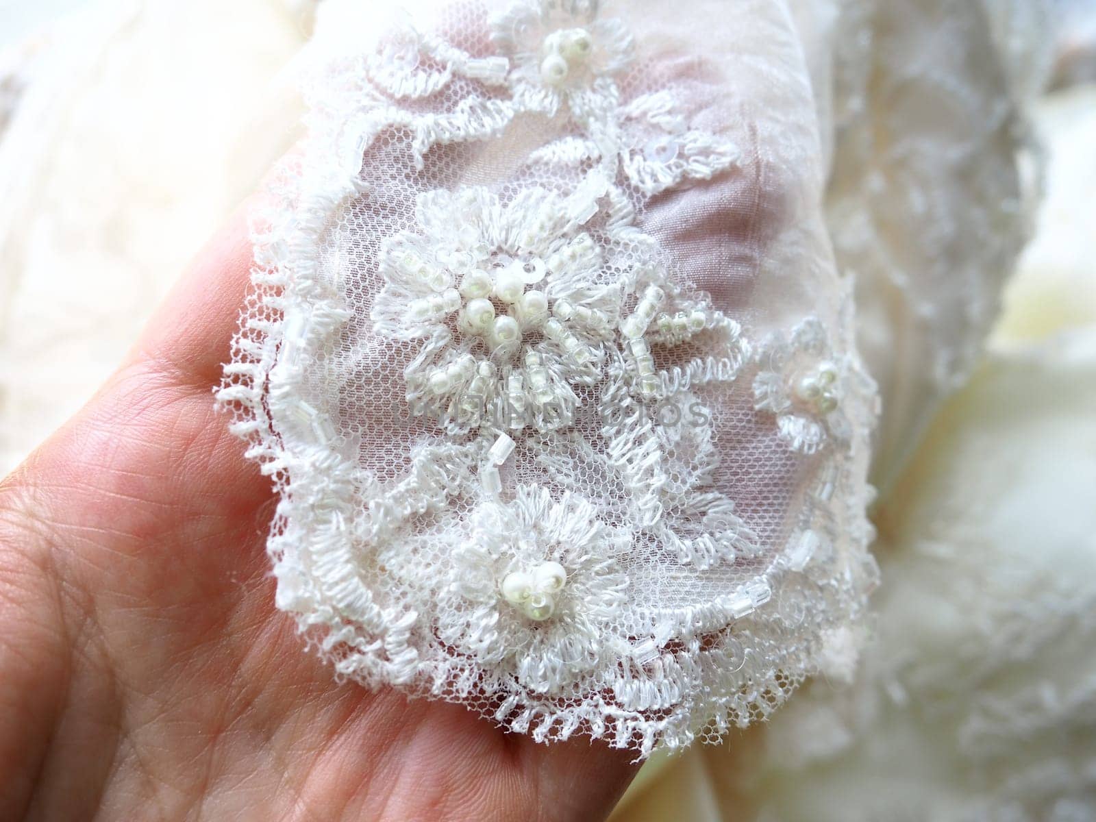 Hand touches beadwork and lace close-up on a white wedding dress. Beautiful jewelry for the bride's outfit. Wedding preparations. Clothes of the newlyweds. Small shiny details on the dress, handmade.