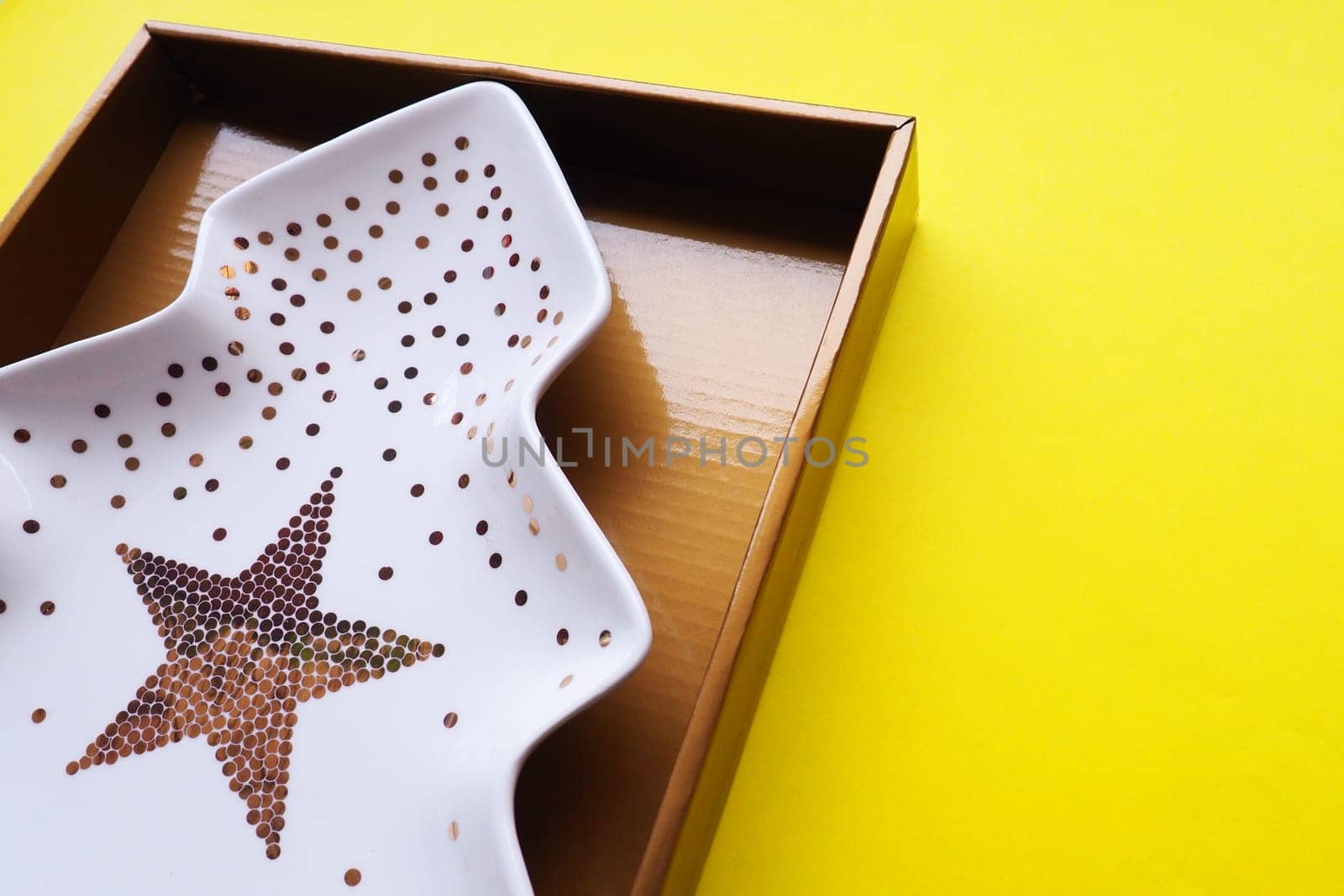 A plate in the shape of a Christmas tree with gold ornaments and a star in the middle. Gift wrapping. Yellow background. New Year Christmas card. Background for advertising and lettering. Copy space