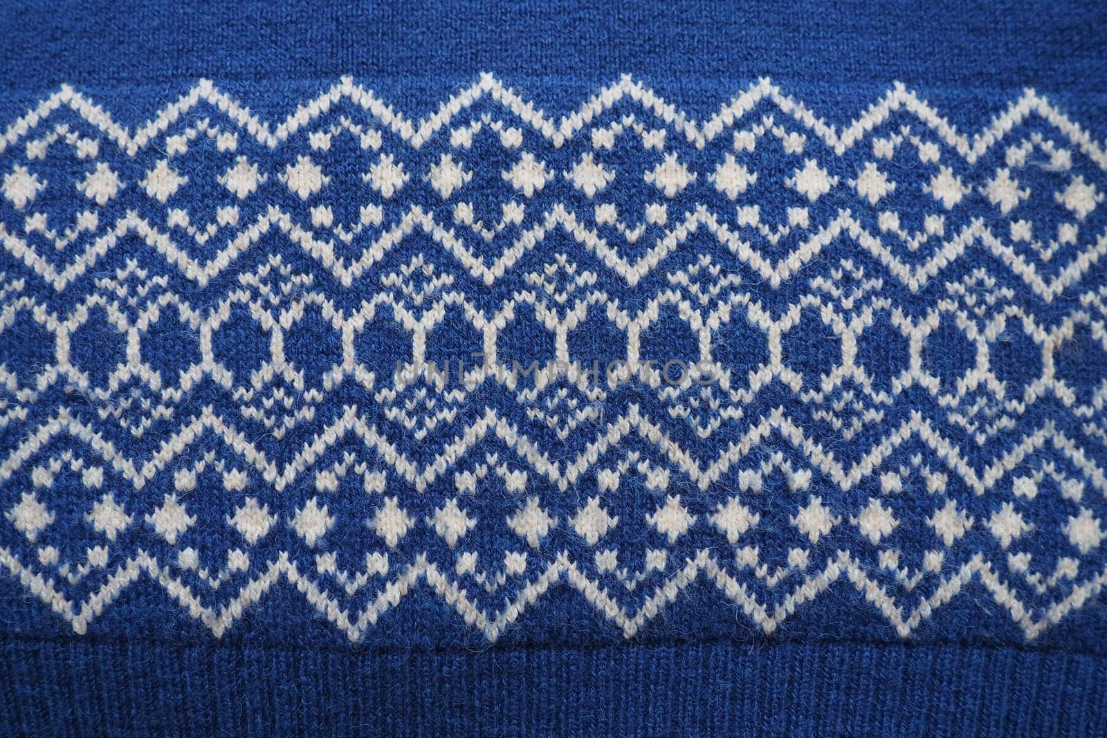 Jacquard knitted pattern. Knitted with white thread rhombuses and zigzags on a blue background. Geometric ornament for Christmas or New Year. Winter trendy modern traditional folk clothing ornament