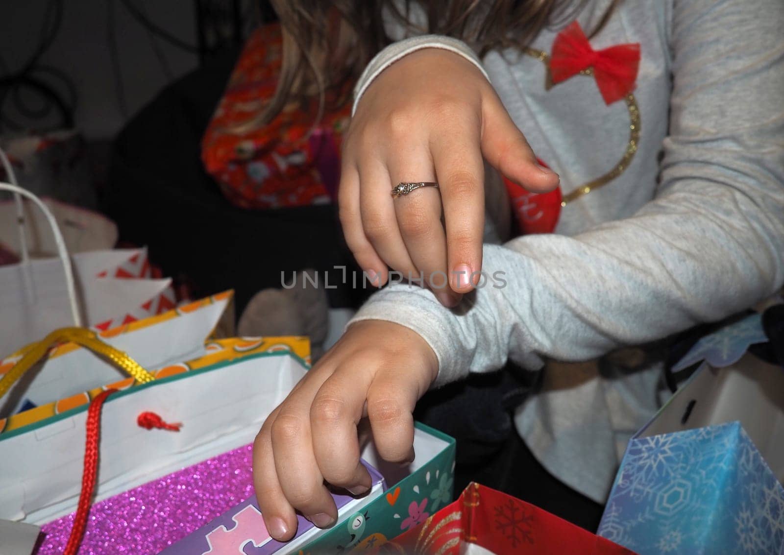Beautiful children's hands open packages with gifts after the birthday celebration. Unpacking sale purchases or items in decorative packaging bags. Gray long sleeves