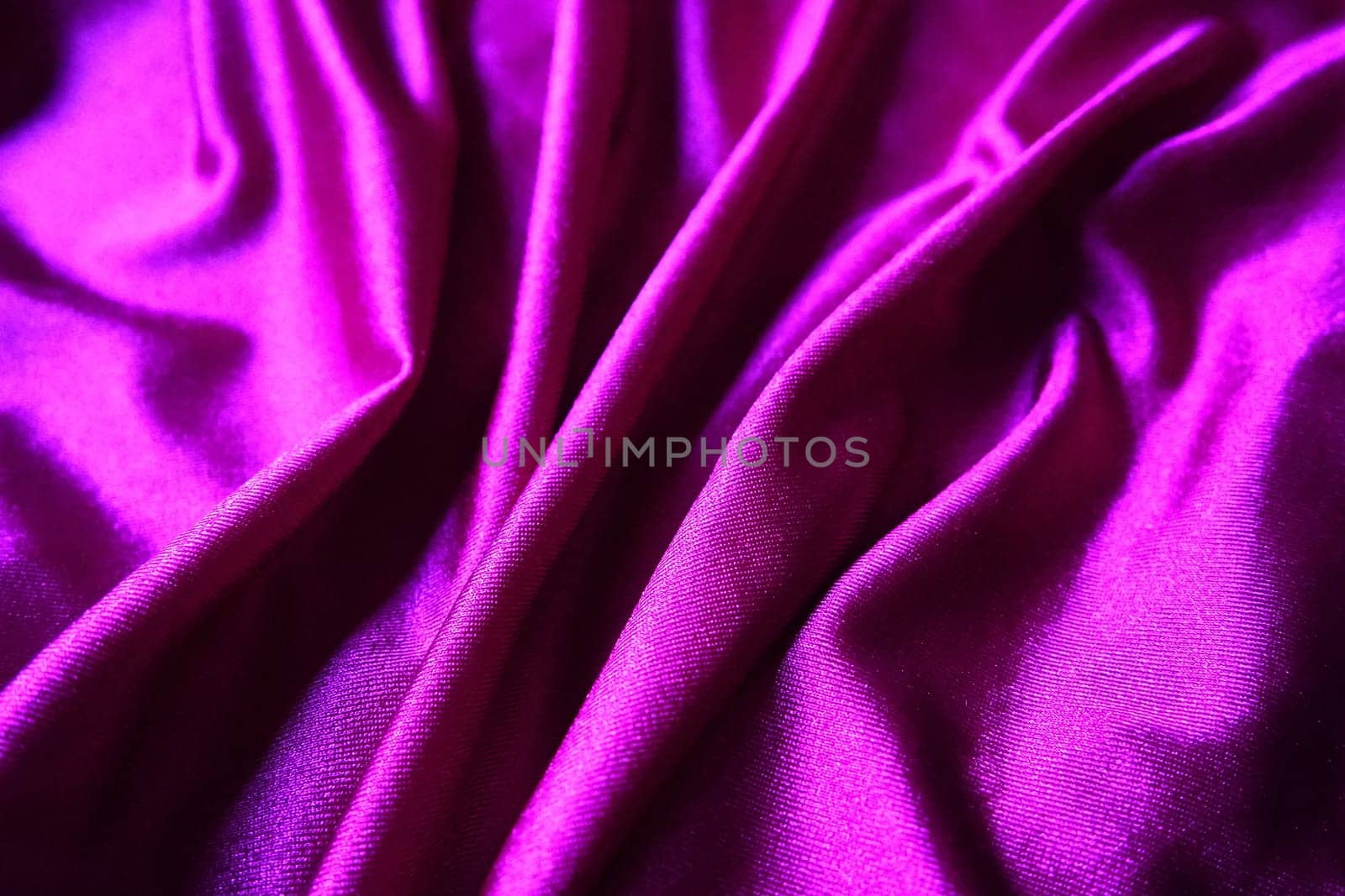 Velour fabric, similar to silk. Textiles in a folds and beautiful waves. Purple, pink, magenta shades on the drapery. Sewing material for evening dresses, furniture upholstery, curtains and interior