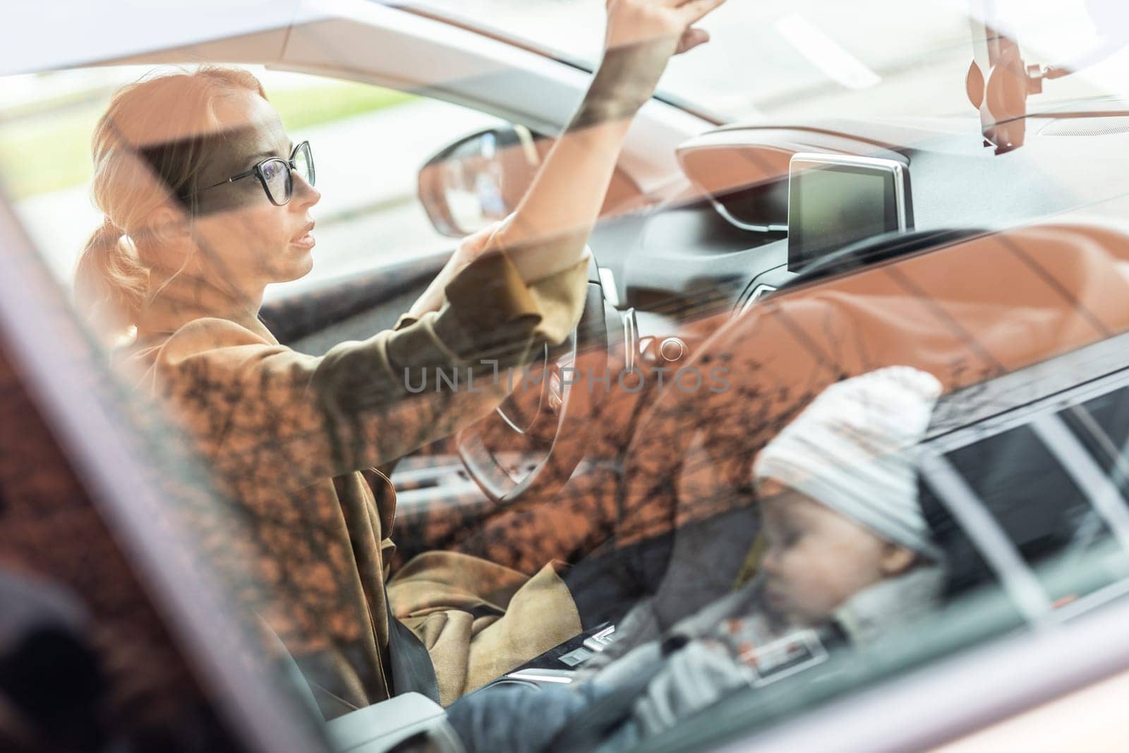 Mother concentrating on driving family car running errands while her baby sleeps in infant car seat by her site