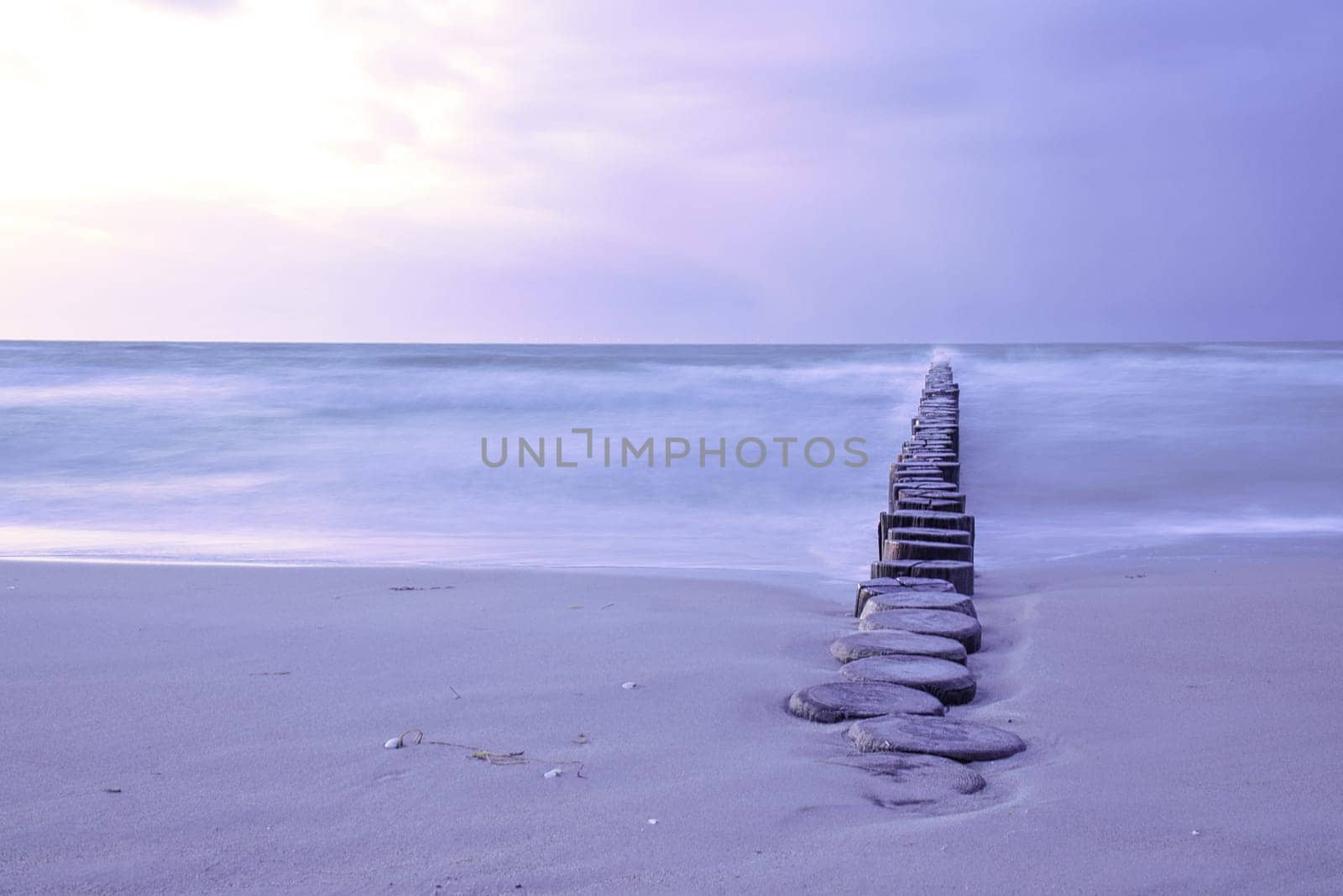 Groynes protruding into the horizon in the Baltic Sea. Long exposure with muted colors. Landscape shot by the sea