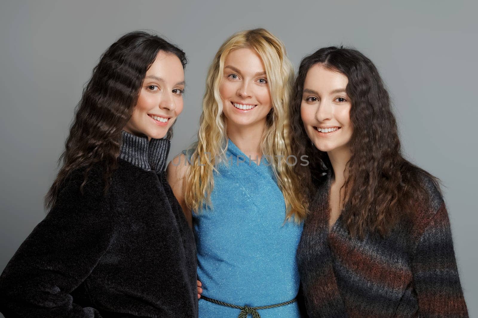 Three attractive girls in woolen coats posing in studio. Happy smiling friends. Natural makeup.