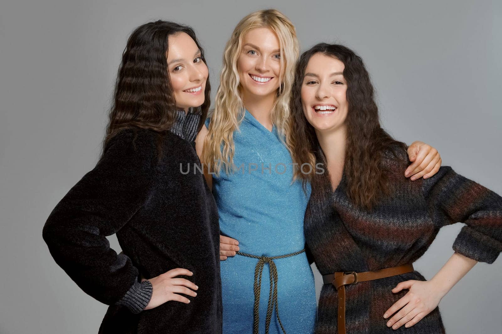 Three attractive girls in woolen coats posing in studio. Happy smiling friends. Natural makeup.