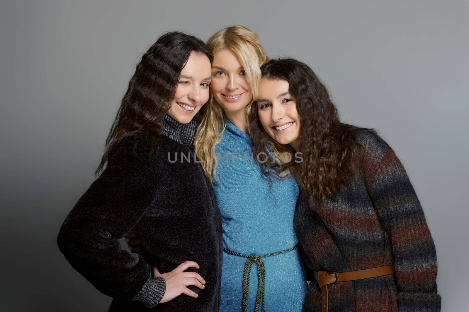 Three attractive girls in woolen coats posing in studio. Happy smiling friends. Natural makeup.
