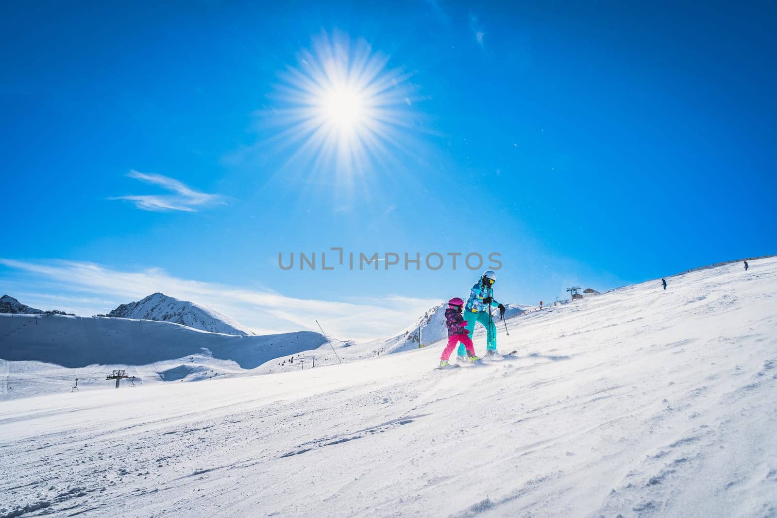 Mother and daughter preparing to descend on a ski slope. Sunny day on ski winter holidays in Andorra, El Tarter, Pyrenees Mountains