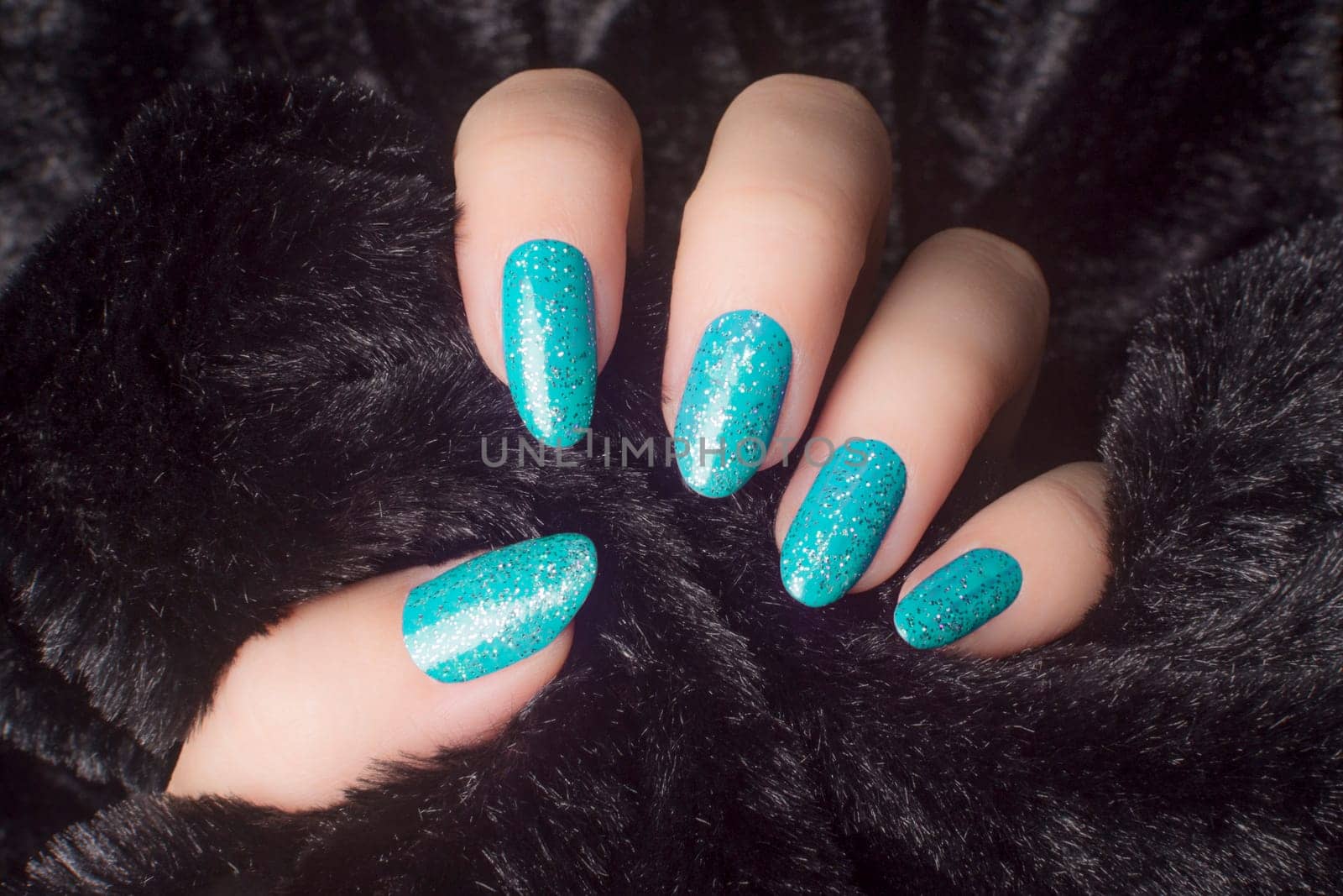 Female hand with glittered white blue nails is holding black fur, manicure and nail care concept.
