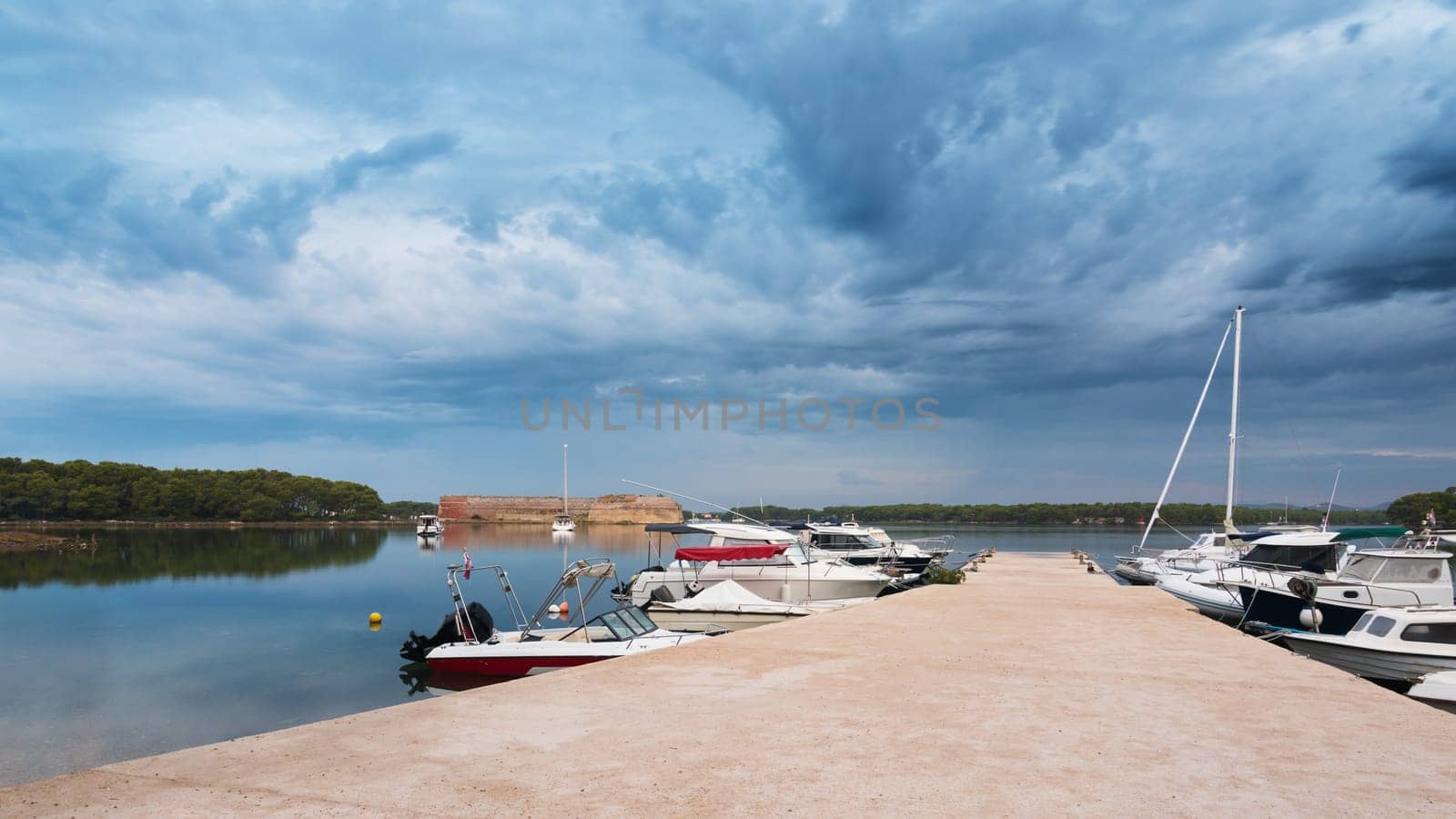 Pier with boats on the bay at sveti nikola fortres with dark clouds, sibenik