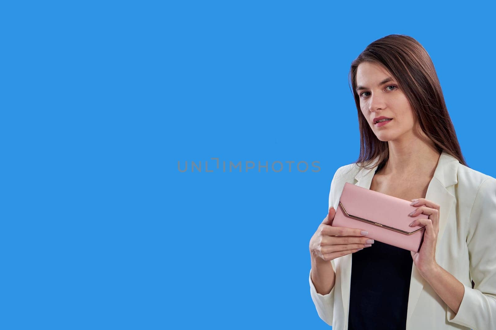 A beautiful young woman is holding a pink purse on a blue background, copy space. High quality photo