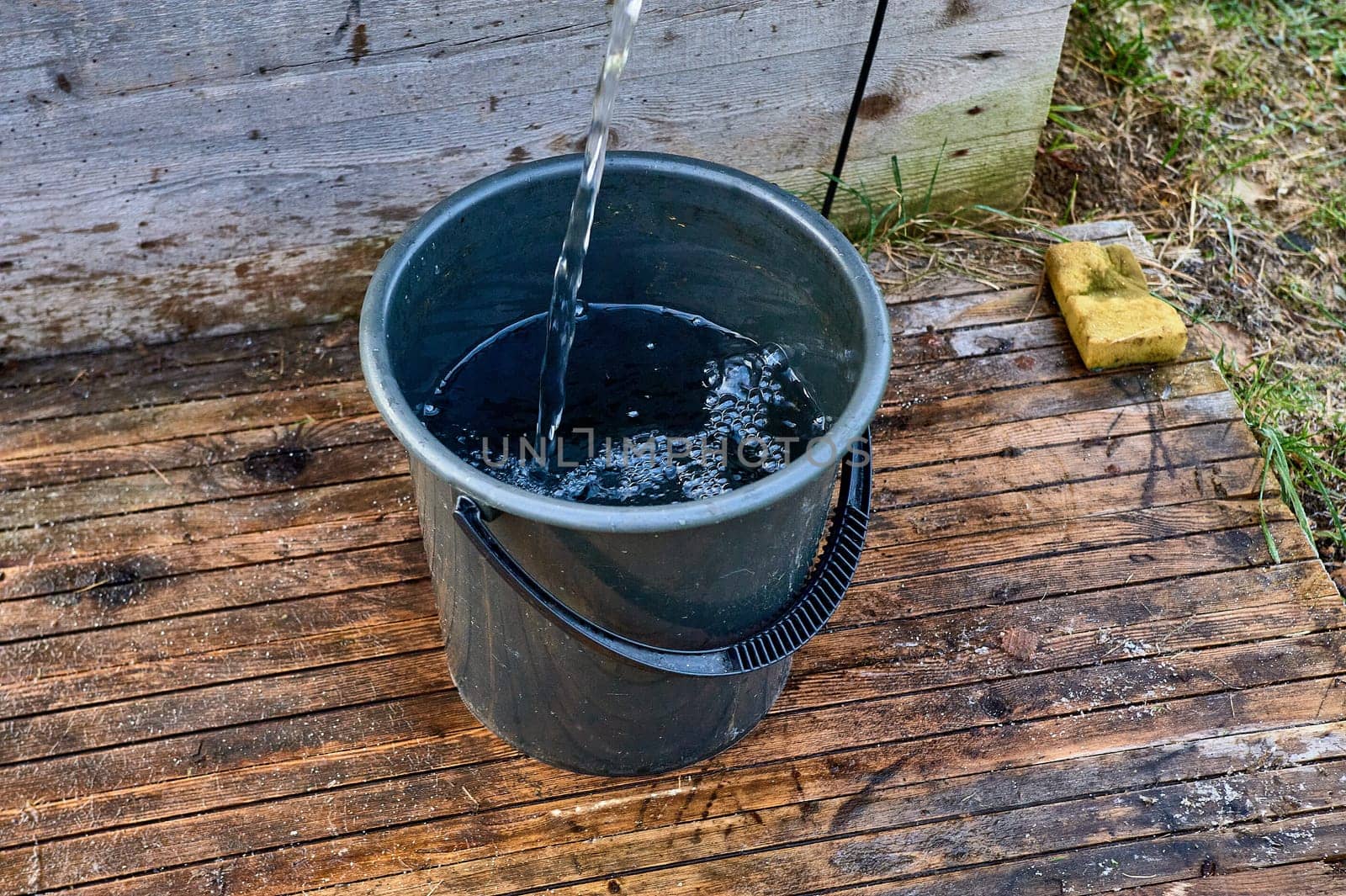 a black plastic bucket is filled with water from the pump. High quality photo