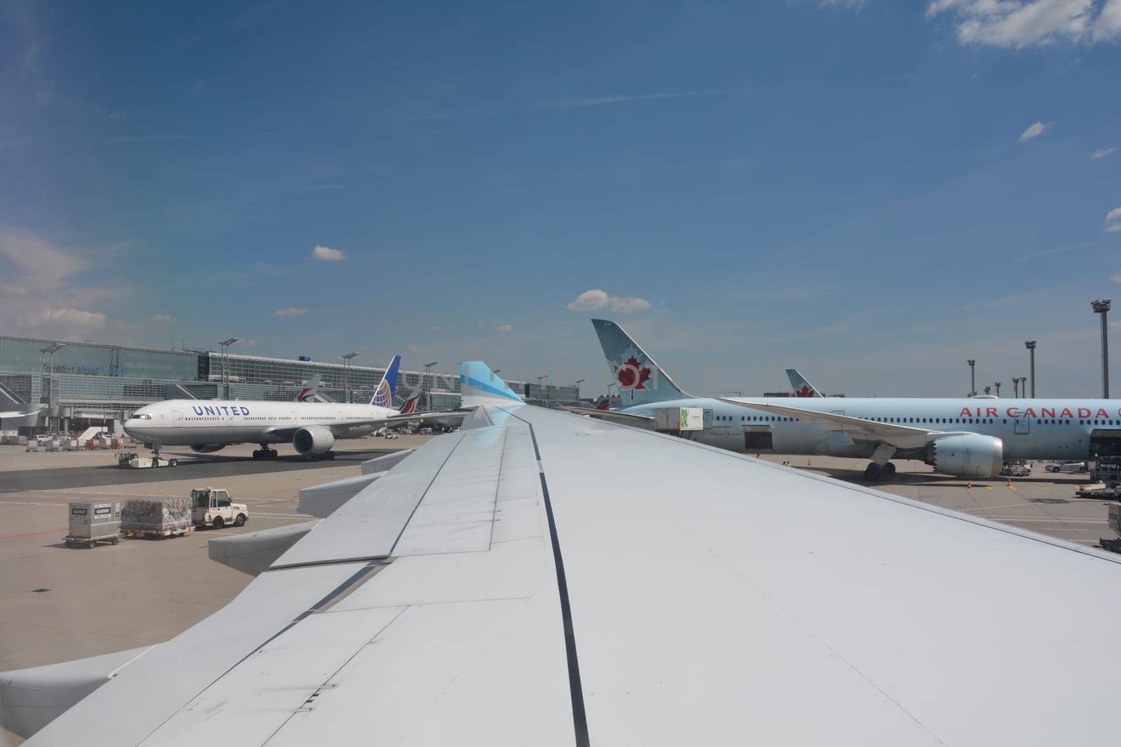 Frankfurt Airport Germany August 02, 2022 - View from the aircraft window onto a wing and a view of the terminal, a United machine being towed to the runway and an Air Canada machine being loaded