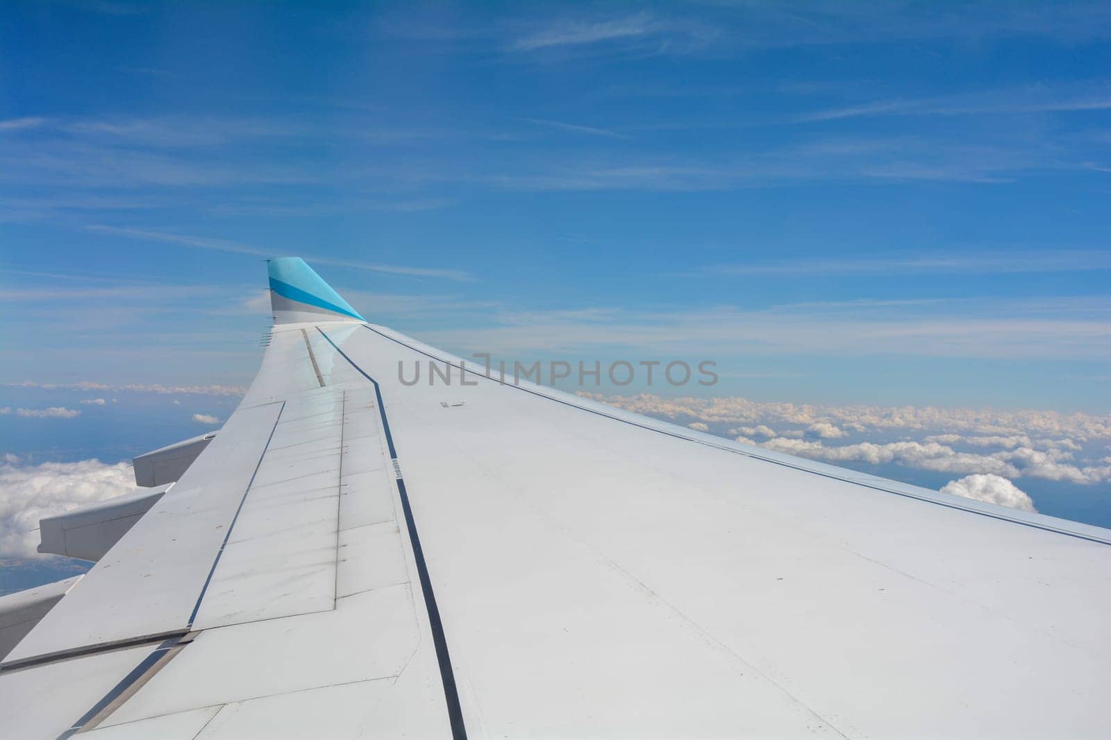 Looking out of an airplane window showing a plane wing with blue sky and white clouds