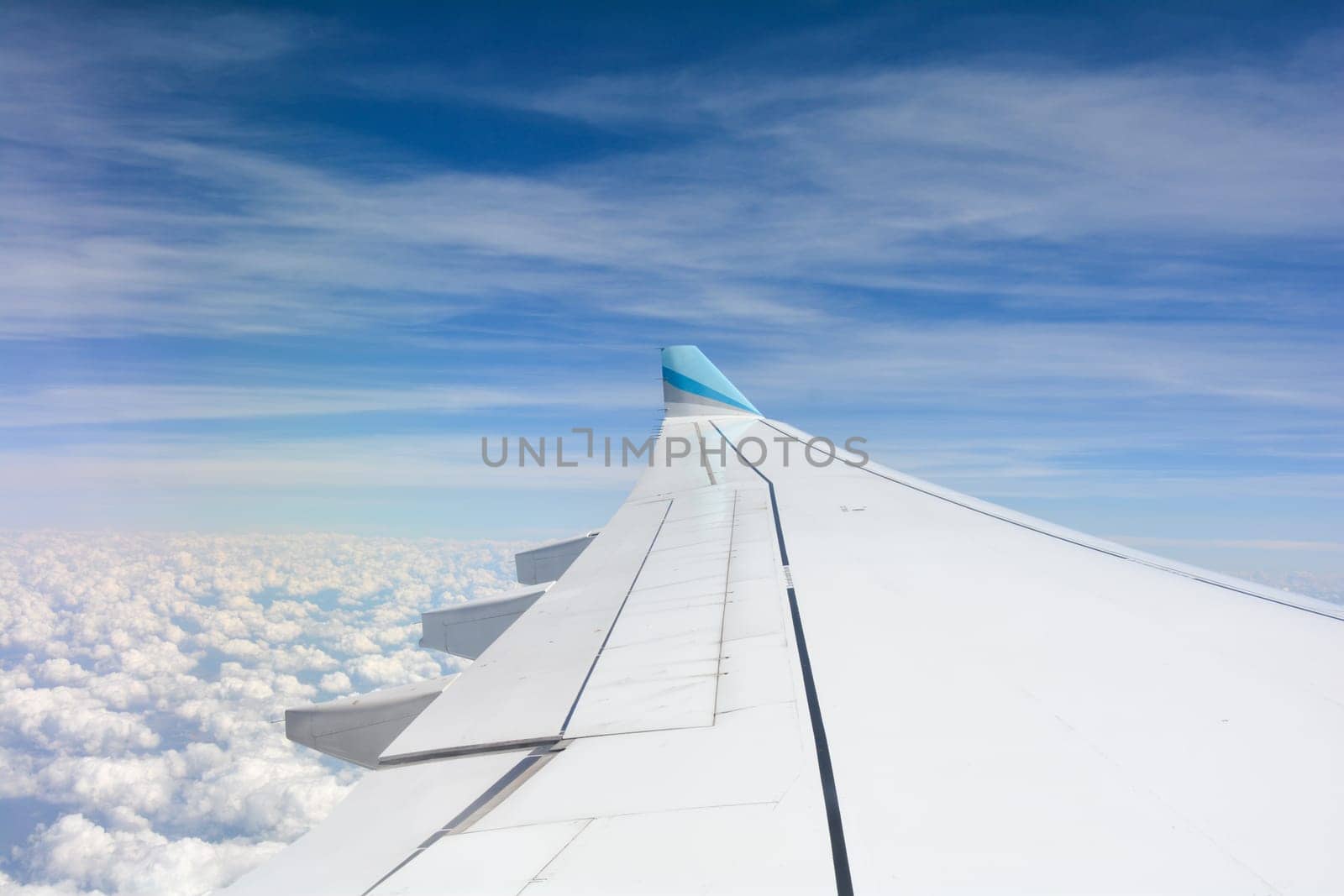 Looking out of an airplane window showing a plane wing with blue sky and white clouds
