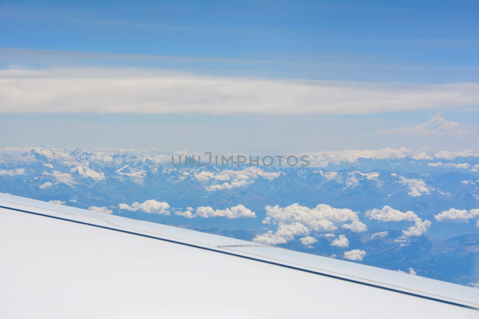 View from an airplane window showing a plane wing, mountains, blue sky and white clouds